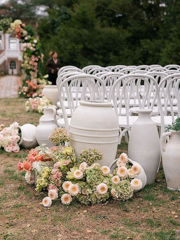 Ceremony aisle decor with outdoor ceremony seating, white bentwood chairs flanking stone path with hydrangea and rose ground florals, floral arch ahead
