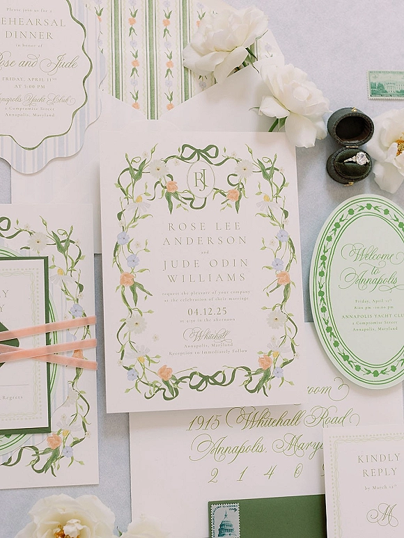 Invitation suite with floral wedding invitation cards, envelopes, ribbon, stamps, and engagement ring on a light gray flat lay background