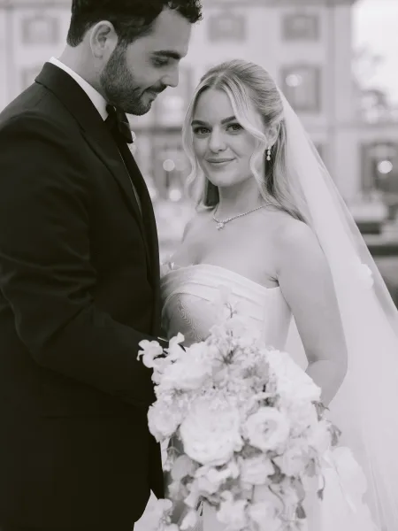 Couple portrait with bride holding bouquet while the groom gazes at her, her veil catching light as they share a quiet moment.