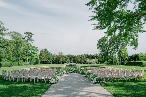 Ceremony setup with circular ceremony seating around a reflecting pool and fountain, white florals lining the gravel path.