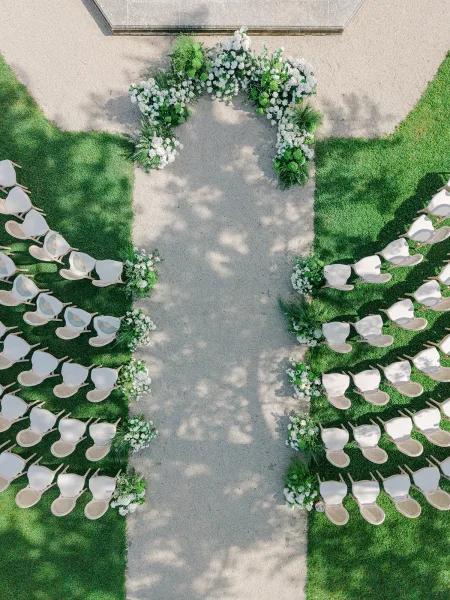 Ceremony aisle design with white florals in an outdoor ceremony setup, lining a gravel path across a grass lawn toward a stone platform.