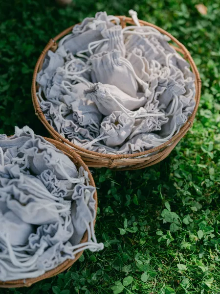 Wedding favor bags neatly displayed in multiple wicker baskets across a grass lawn dotted with clover leaves.