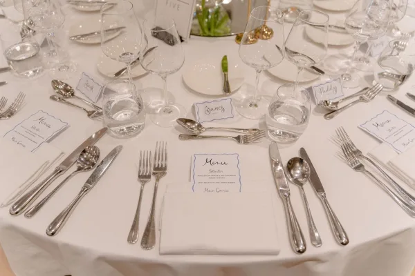 Wedding table setting with elegant reception place setting, featuring menu cards on a crisp white tablecloth at a round table.