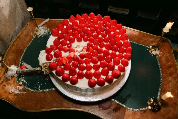 Wedding cake with white frosting, a strawberry wedding cake crowned with whole strawberries, rests on a wooden table with green leather inlay.