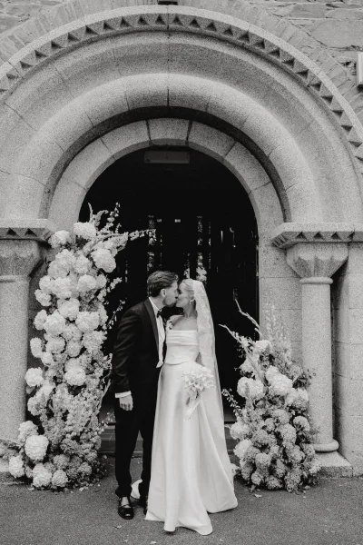 Wedding kiss portrait of the couple beneath a stone church arch, a church wedding portrait with her lace veil gently trailing.