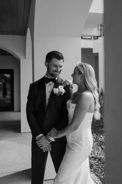 Couple portrait in a black and white wedding portrait style, bride holding groom’s arm and showing her ring under arched corridor walkway