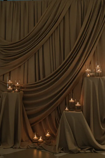 Wedding backdrop decor with draped fabric wedding backdrop, pedestal stands and candle clusters in glass cylinder vases on a tiled floor