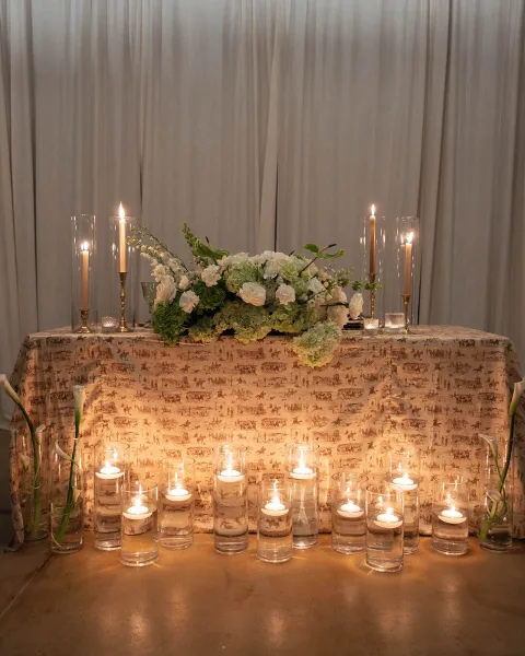 Sweetheart table decor with a floating candle display and white and green florals before draped curtains.
