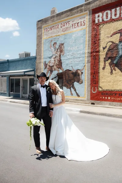 Couple portrait, a mural wall portrait on the street, with the groom in a cowboy hat standing beside his bride.