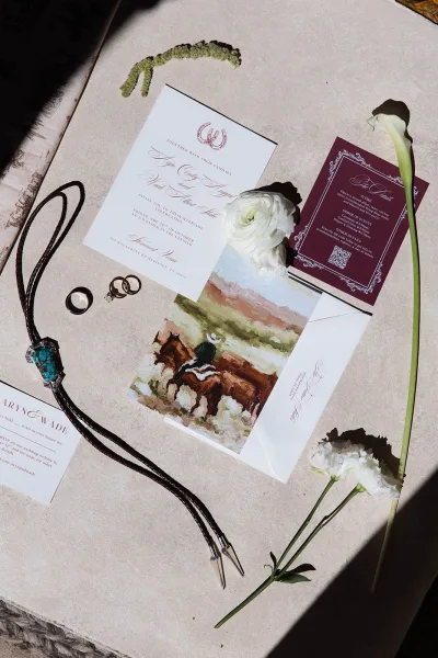 Wedding invitation suite designed as western wedding invitations, paired with a turquoise bolo tie on a stone tabletop, in serif and script.