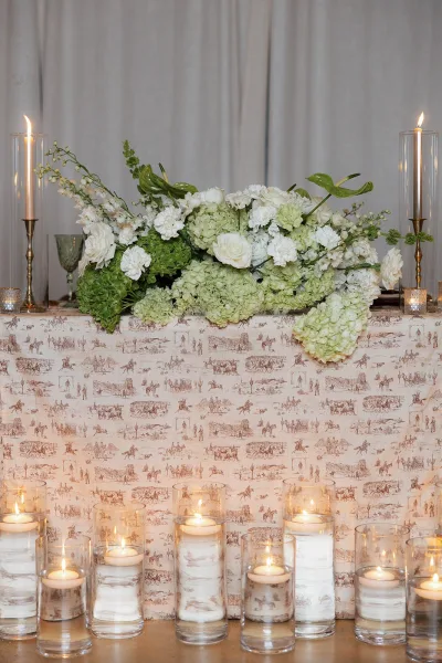 Reception table decor with sweetheart table flowers in a soft, romantic arrangement, highlighted by gold candlesticks.