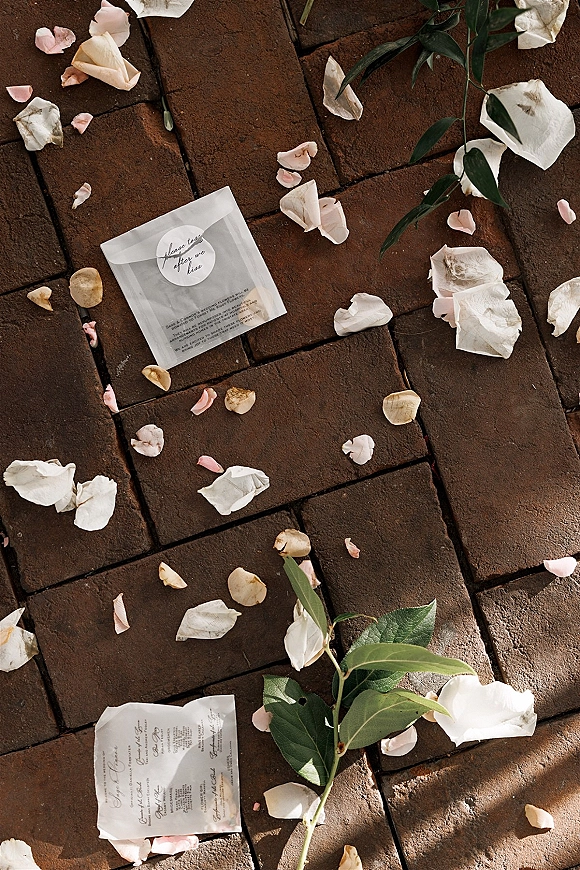 Wedding favor bag in clear wedding favor packaging with round sticker and dried rose petal confetti, styled on a brick paver walkway