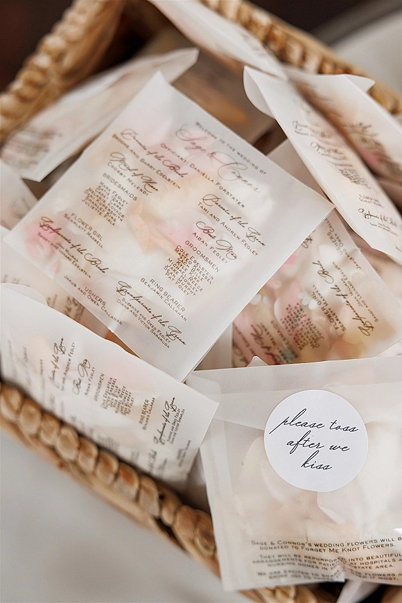 Wedding programs with ceremony program design in vellum paper, calligraphy text and ribbon, arranged in a woven basket on a tabletop