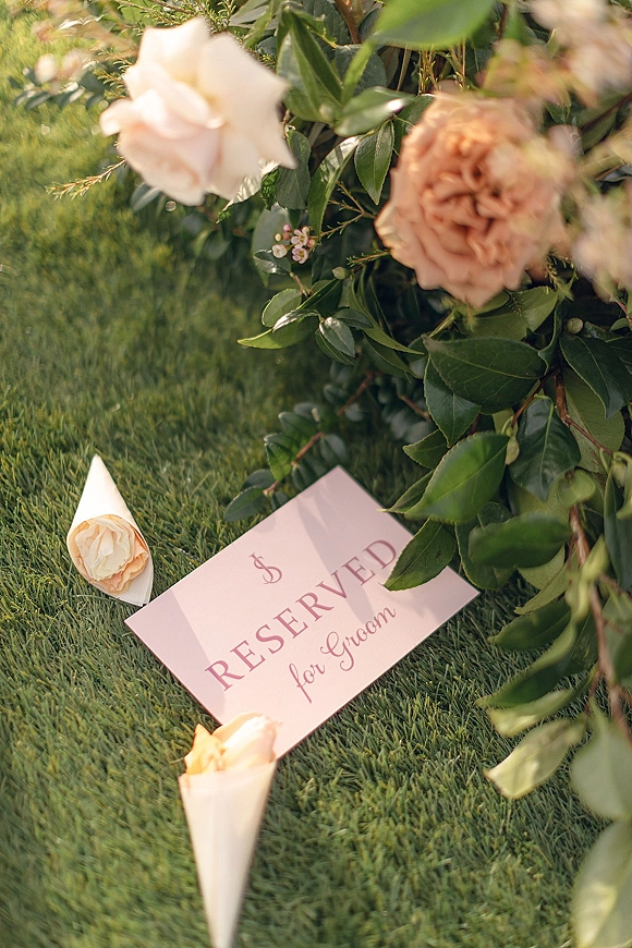 Wedding reserved sign with a reserved seat card and blush flowers with greenery on a chair beside paper cones on a grass lawn