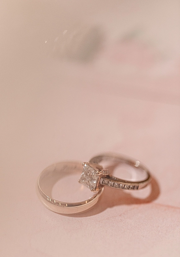 Wedding rings with an engagement ring close up featuring a square diamond on white fabric, metal bands stacked in soft light