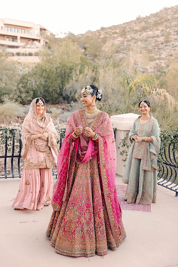 Bride portrait of an Indian bride in a pink embroidered lehenga with gold jewelry and dupatta, standing on a terrace with mountain views