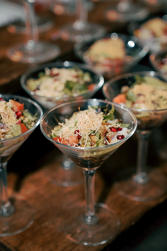 Wedding appetizer cups served in martini glass appetizer style, layered salad ingredients topped with shredded cheese on a wood table