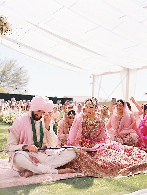 Wedding ceremony moment at a south asian wedding ceremony as the groom wipes tears beside the bride in a pink lehenga under a canopy tent
