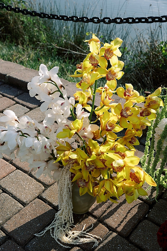 Wedding floral arrangement with yellow orchids and hanging amaranthus in a ceramic vase on a brick patio by the lakeshore