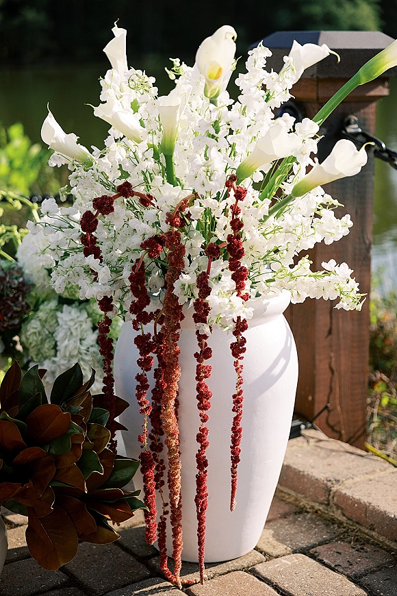 Wedding floral arrangement with calla lily centerpiece of white calla lilies, sweet peas, and burgundy amaranthus in a white ceramic vase by a lake railing
