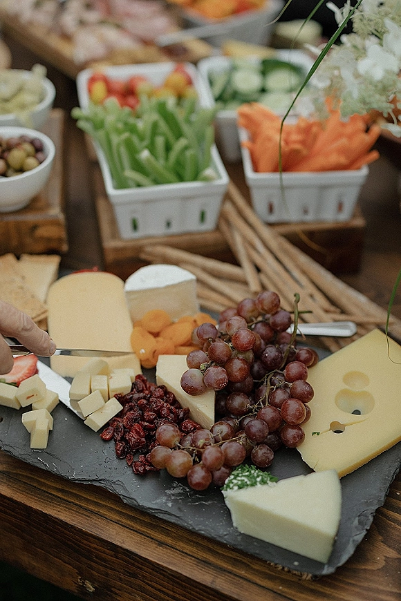 Wedding charcuterie board with wedding cocktail hour snacks including cheese, grapes, dried fruit, crackers, breadsticks, and crudites on a buffet table