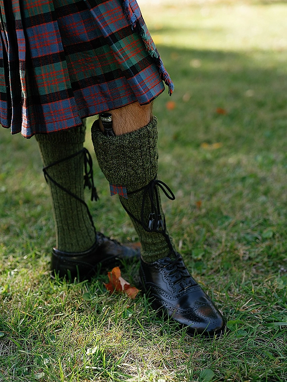 Groom kilt outfit with tartan wedding kilt, sporran, kilt hose and garter flashes, and black brogue shoes on a grassy lawn with fallen leaves