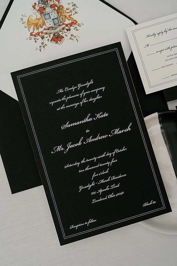 Wedding invitation suite with black and white wedding invitations, calligraphy crest card, RSVP, white envelope liner, and wax seal on ribboned table