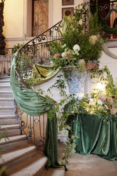 Staircase wedding decor with wedding staircase greenery draped in green fabric, hydrangea florals and garland along wrought iron railing in foyer