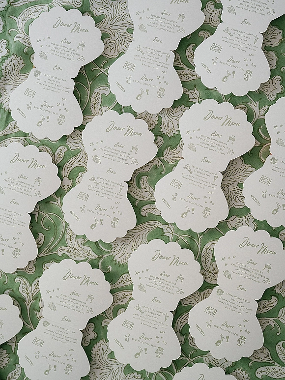 Wedding menu cards with scalloped wedding menu edges, printed calligraphy and food icons on green patterned fabric background