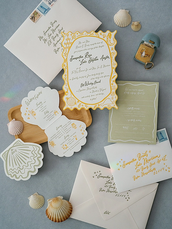 Invitation suite wedding invitation flat lay with scalloped cards, wax-sealed envelopes, vintage stamps, seashells, and ring on blue linen