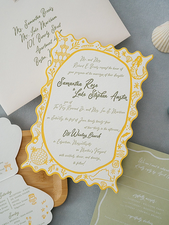 Wedding invitation suite with scalloped wedding invitation, gold and green ink, envelope, RSVP and details cards on gray fabric with shell accent
