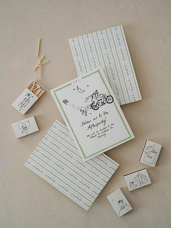 Wedding invitation suite with illustrated wedding invitations, patterned envelopes, matchbox and stamp blocks arranged on linen fabric flat lay