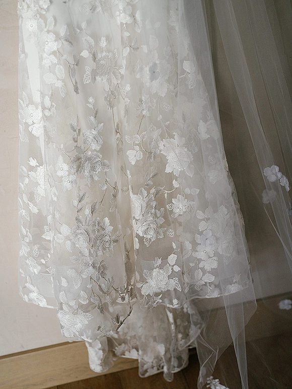 Wedding dress detail featuring lace wedding dress floral appliqué and beaded embroidery on a tulle skirt hem against an indoor wall and wooden floor