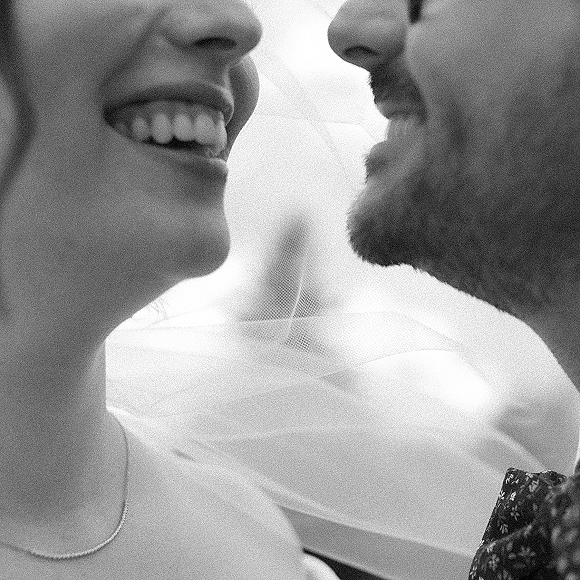 Wedding kiss portrait of bride and groom close up, laughing cheek to cheek under a bridal veil against a soft light backdrop