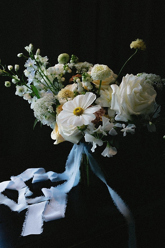 Bridal bouquet of white wedding bouquet blooms and greenery tied with a blue ribbon, trailing ribbons flowing against a dark backdrop