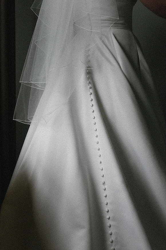 Wedding dress close-up of a wedding dress button back with covered buttons and a tulle veil cascading over smooth fabric against a dark backdrop