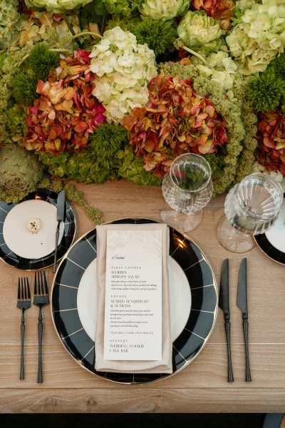 Wedding place setting on a reception tablescape, with a custom menu card centered on the plate atop a wood tabletop.