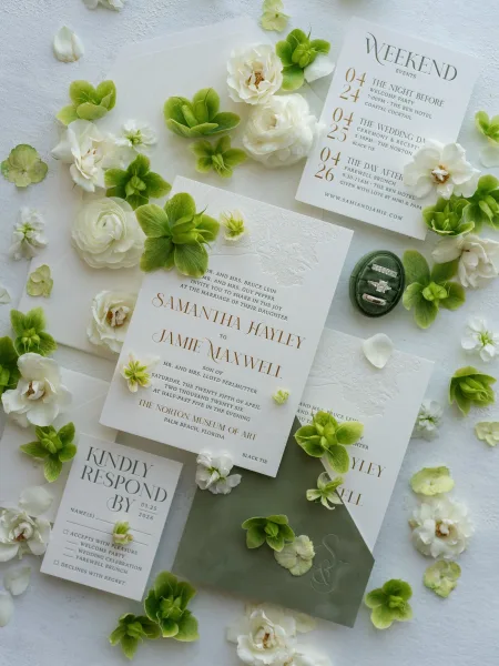 Wedding invitation suite featuring green and white invitations with a velvet ring box, styled on linen fabric.