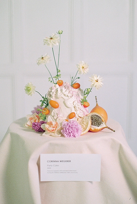 Wedding cake with floral wedding cake topper, kumquats, sliced citrus, and buttercream swirls on linen table before white draped backdrop