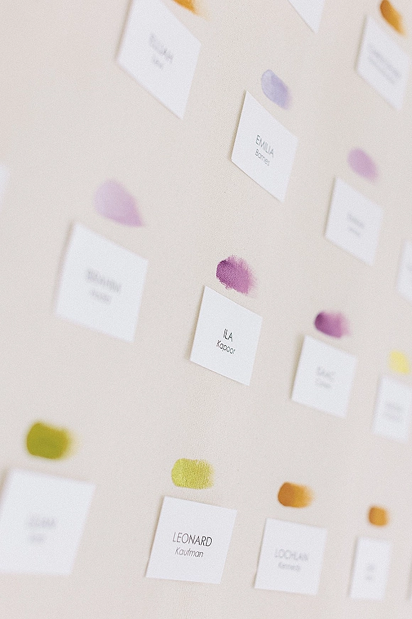 Seating chart with wedding seating chart ideas shown in rows of paper name cards with watercolor swatches on a white board wall display