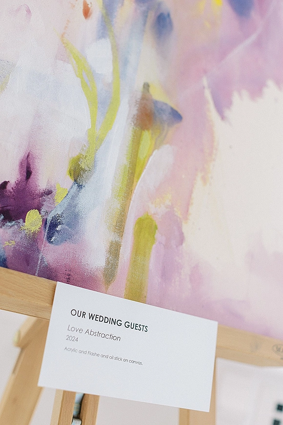 Wedding guest book alternative wedding guest book featuring an abstract painting on an easel with a printed sign card in a blurred indoor setting