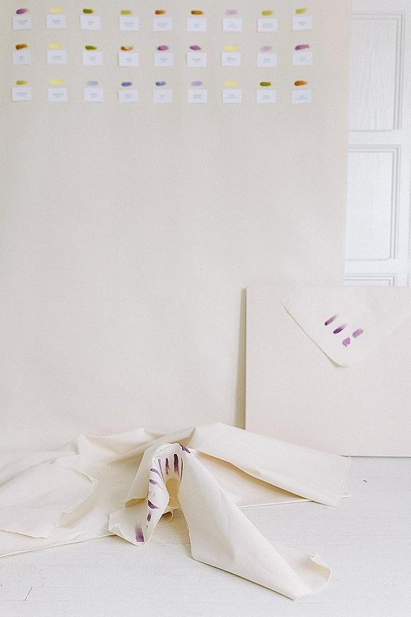 Seating chart display with wedding escort cards taped to a white wall, each card marked with colored dot stickers above a white floor
