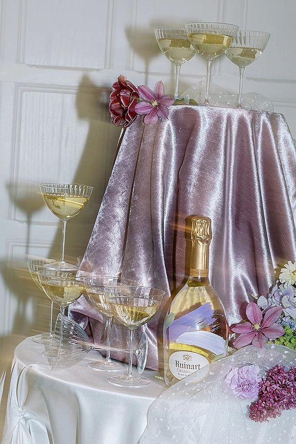 Champagne display with wedding champagne station styling, featuring coupe glasses, a gold bottle, and lilac velvet drape against a paneled wall
