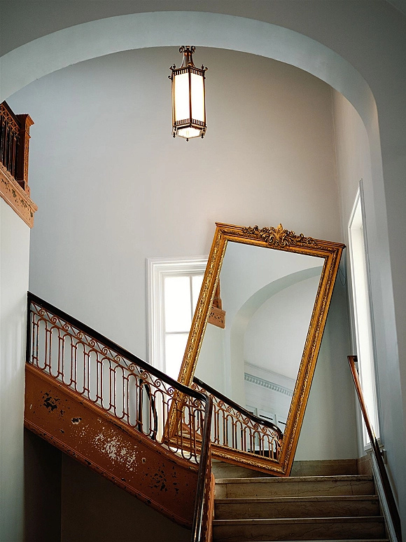 Wedding venue interior with a staircase wedding photo spot, featuring an ornate gold mirror near stone steps in an arched hallway