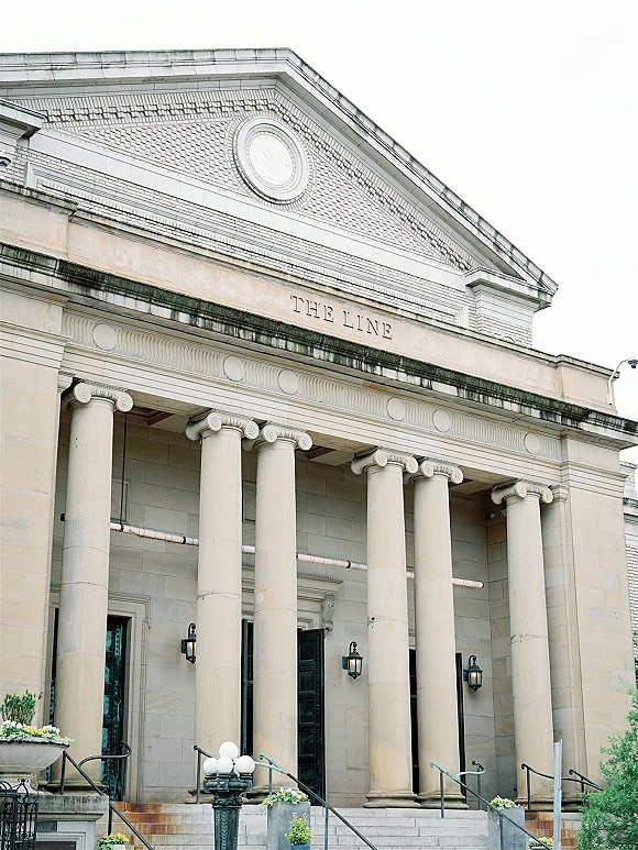 Wedding venue exterior with classic wedding venue facade, featuring tall columns, stone steps, wall lanterns, and planters against a brick pediment roofline
