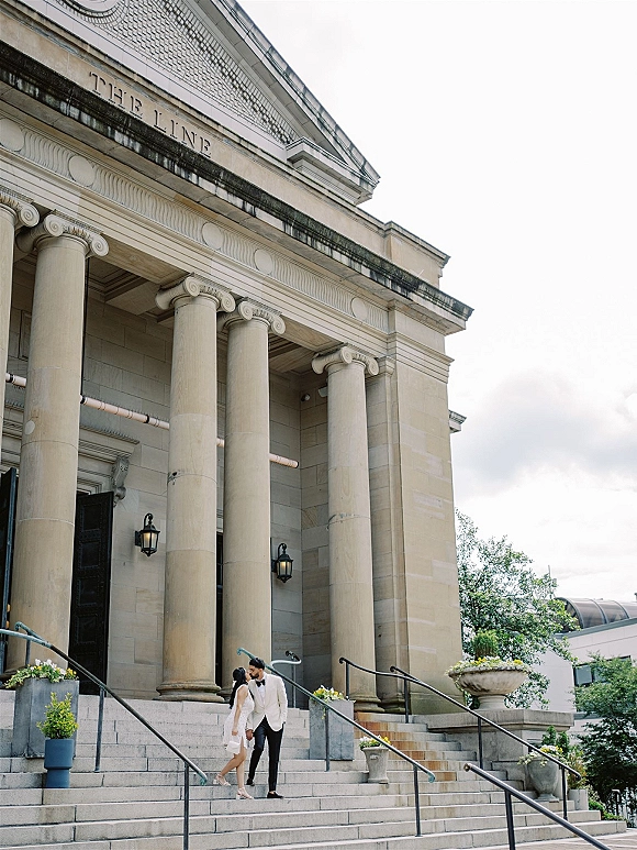 Couple portrait of bride and groom kissing on stone steps outside a neoclassical building, bride in short dress and heels, groom in tuxedo