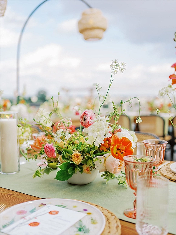 Reception tablescape with wedding table centerpiece in ceramic vase, greenery runner, taper candles, pink goblets under an outdoor tent canopy