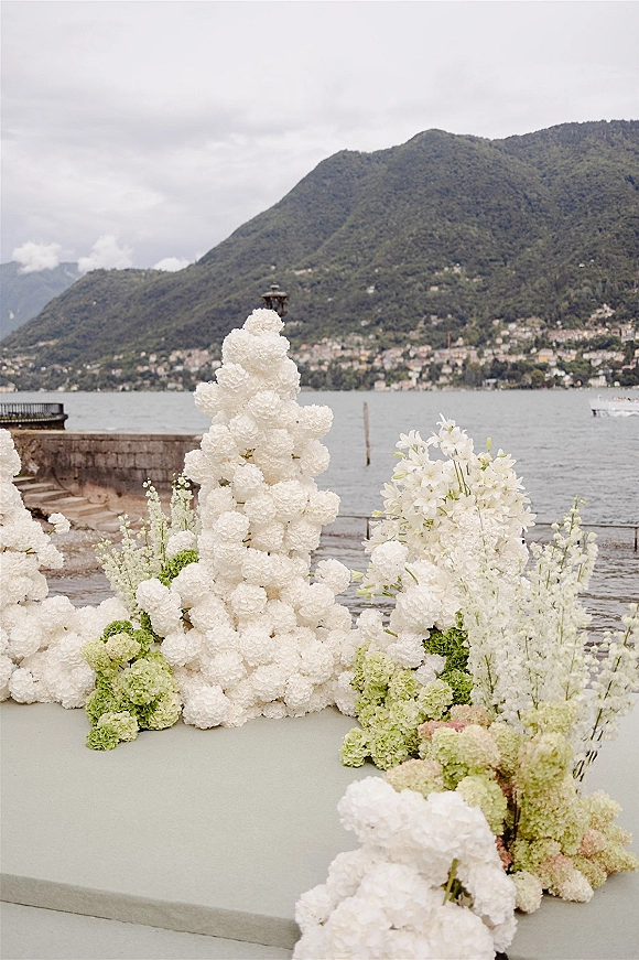Wedding floral arrangement of white wedding florals and green hydrangea in a large installation on a stone terrace by a lakeside mountain view