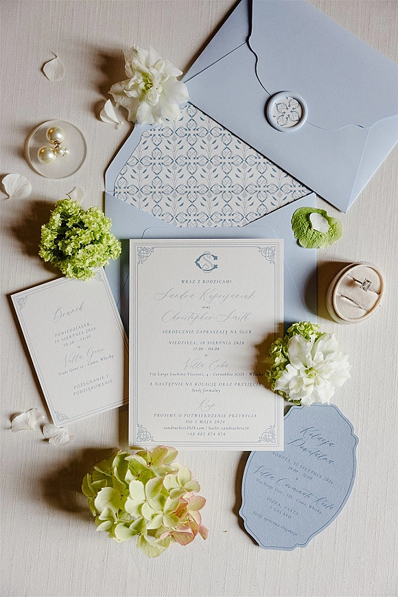 Wedding invitation suite with blue wedding invitations in pastel envelopes, wax seal, rings and pearl earrings on linen with petals