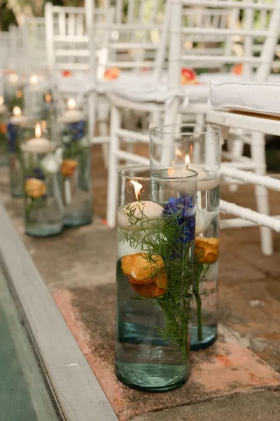 Ceremony aisle decor with floating candle centerpieces in glass cylinder candle holders, roses and greenery lining a stone walkway by white chairs